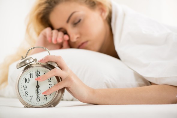 Young woman lying in bed in the morning. She is waking up with alarm clock.